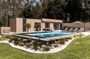 Una casa moderna con piscina, mobiliario exterior y un jardín bien cuidado.