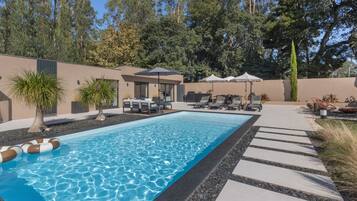 A swimming pool with lounge chairs and umbrellas, surrounded by a landscaped garden and a modern building.
