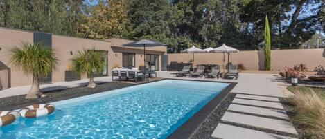 A swimming pool with lounge chairs and umbrellas, surrounded by a landscaped garden and a modern building.
