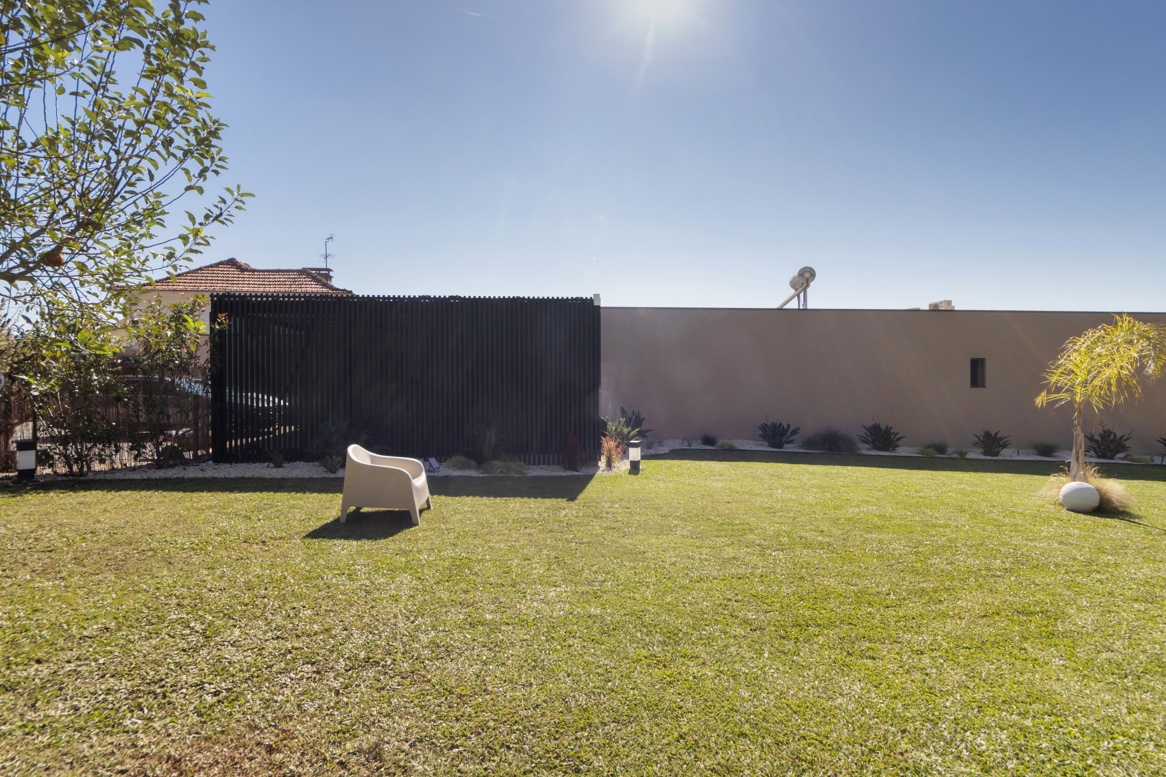 Un espacio al aire libre con césped, una silla blanca, una valla negra y un edificio con tejado de baldosas.