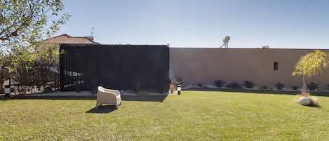 Un espacio al aire libre con césped, una silla blanca, una valla negra y un edificio con tejado de baldosas.