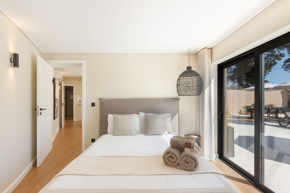 A modern bedroom with a large bed, a hanging light fixture, and a view of the outdoors.