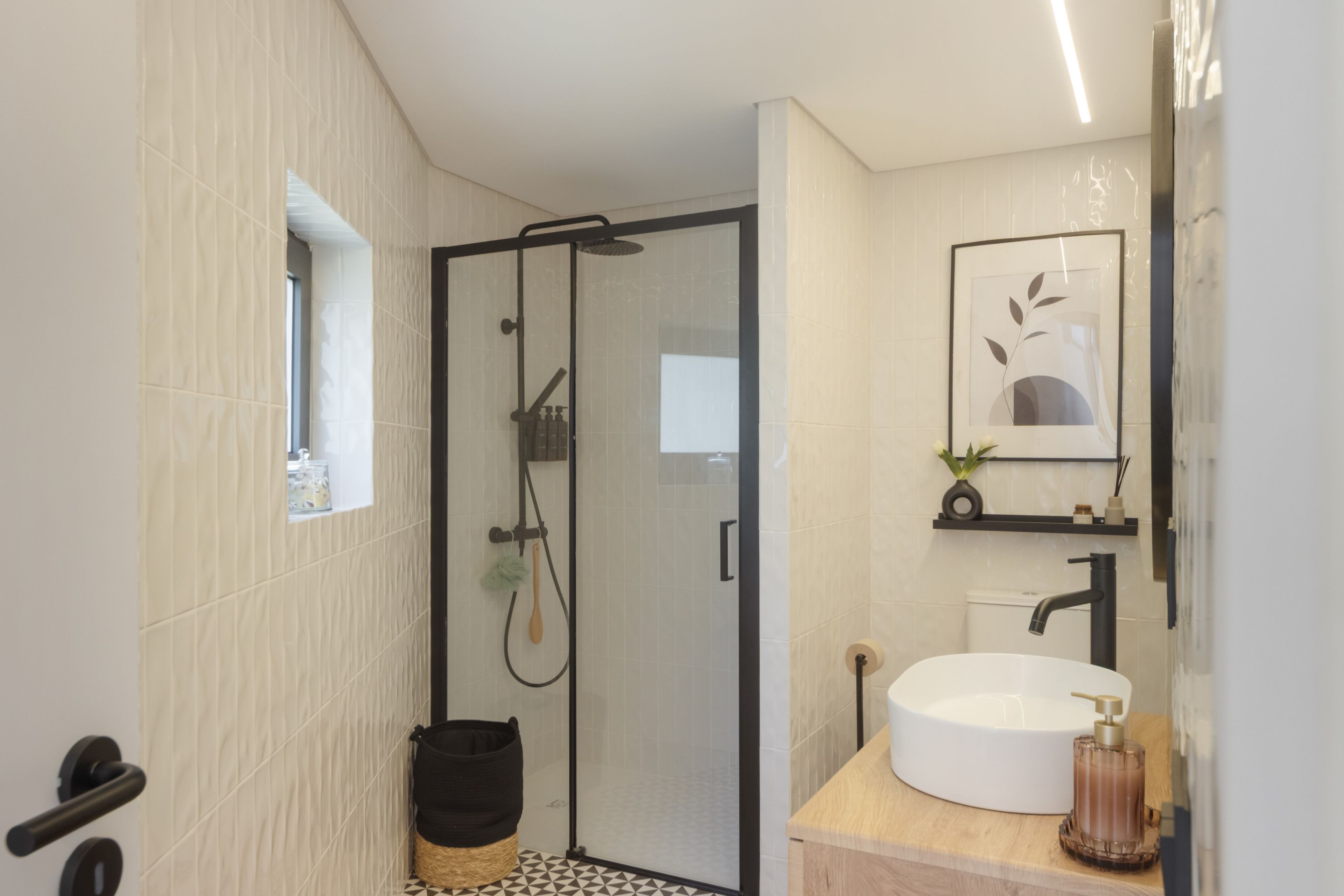 A modern bathroom with a glass-enclosed shower, a white sink, and a framed artwork above the mirror.