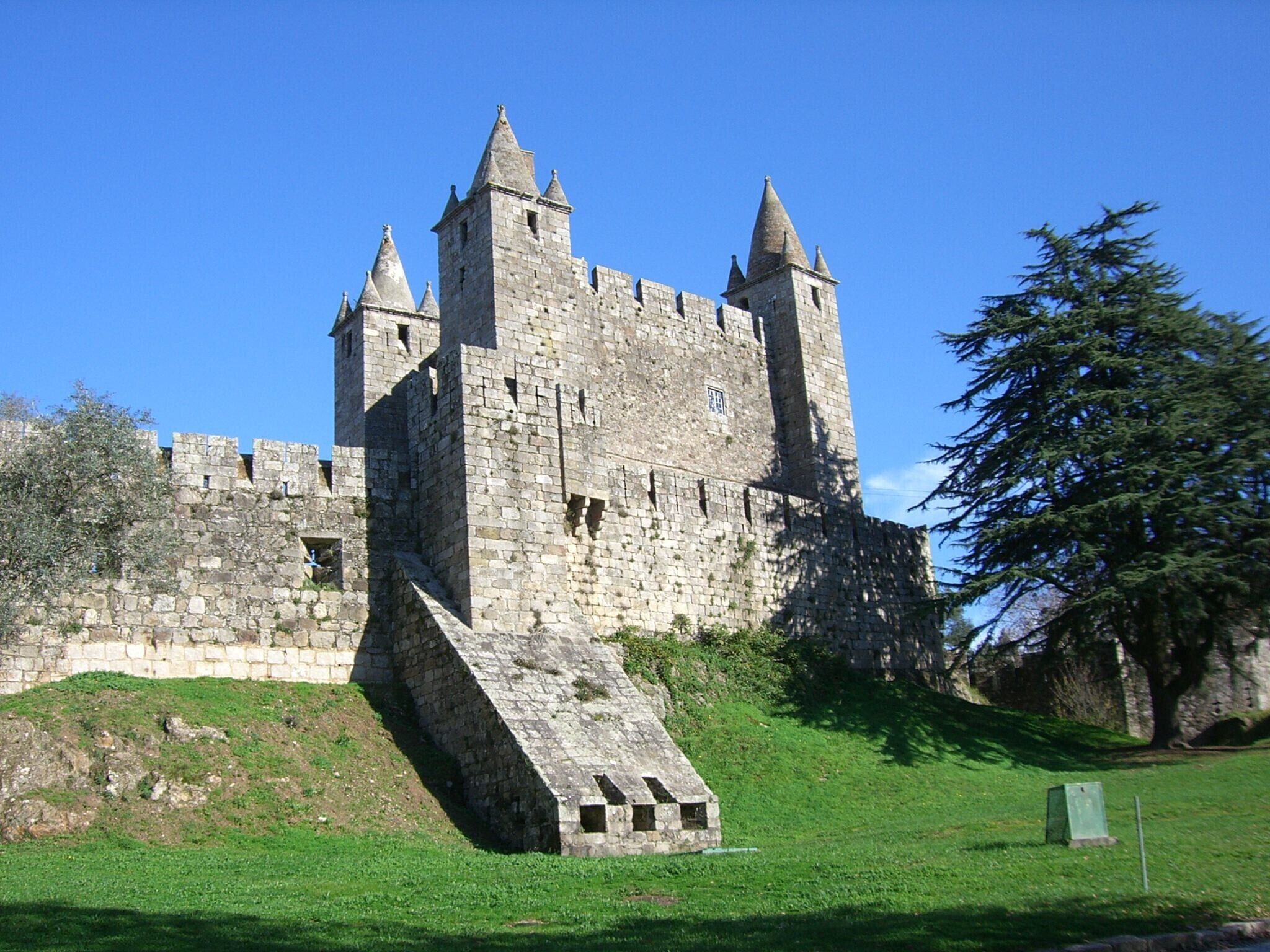 Een historisch stenen kasteel met meerdere torens, een centrale binnenplaats en een gazon op de voorgrond.