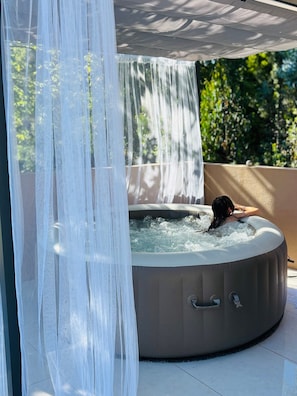 Jacuzzi con una persona relajándose, rodeado por un toldo blanco y una fuente de agua.