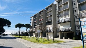 A multi-story residential building with balconies, a clear sky, and a street with trees. - Sea view apartment in central Bibione (Bibione)