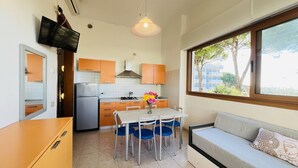 A compact kitchen with a dining area, a sofa, and a TV mounted on the wall. - Sea view apartment in central Bibione (Bibione)