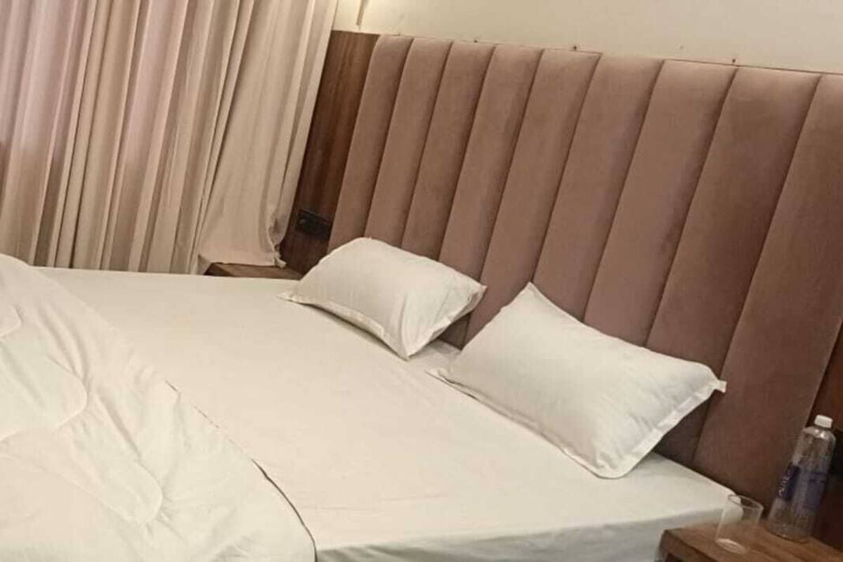 A neatly made bed with white bedding, a wooden headboard, and a bedside table with a bottle.