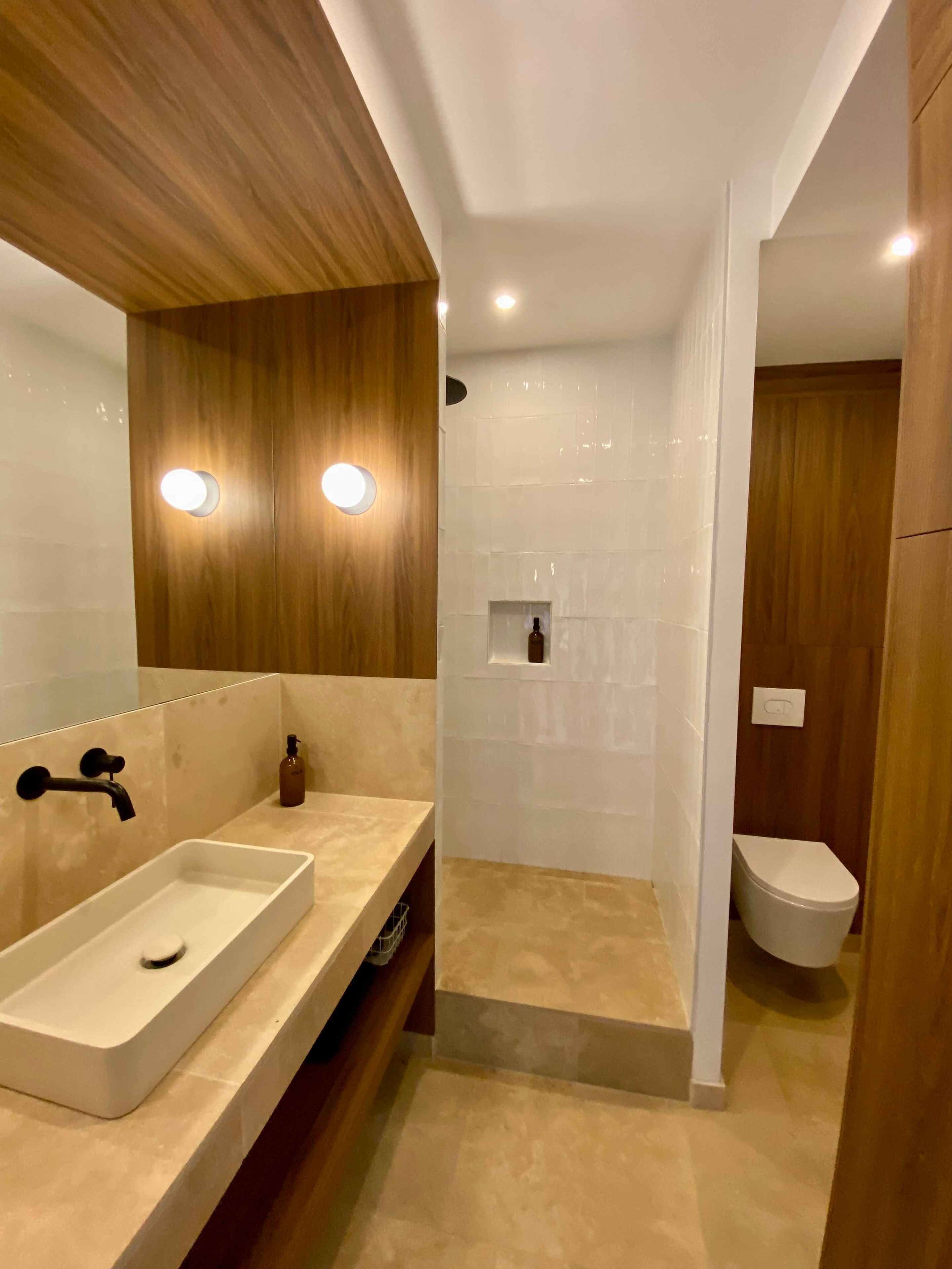 A modern bathroom with a large mirror, a rectangular sink, a shower enclosure, and a toilet.