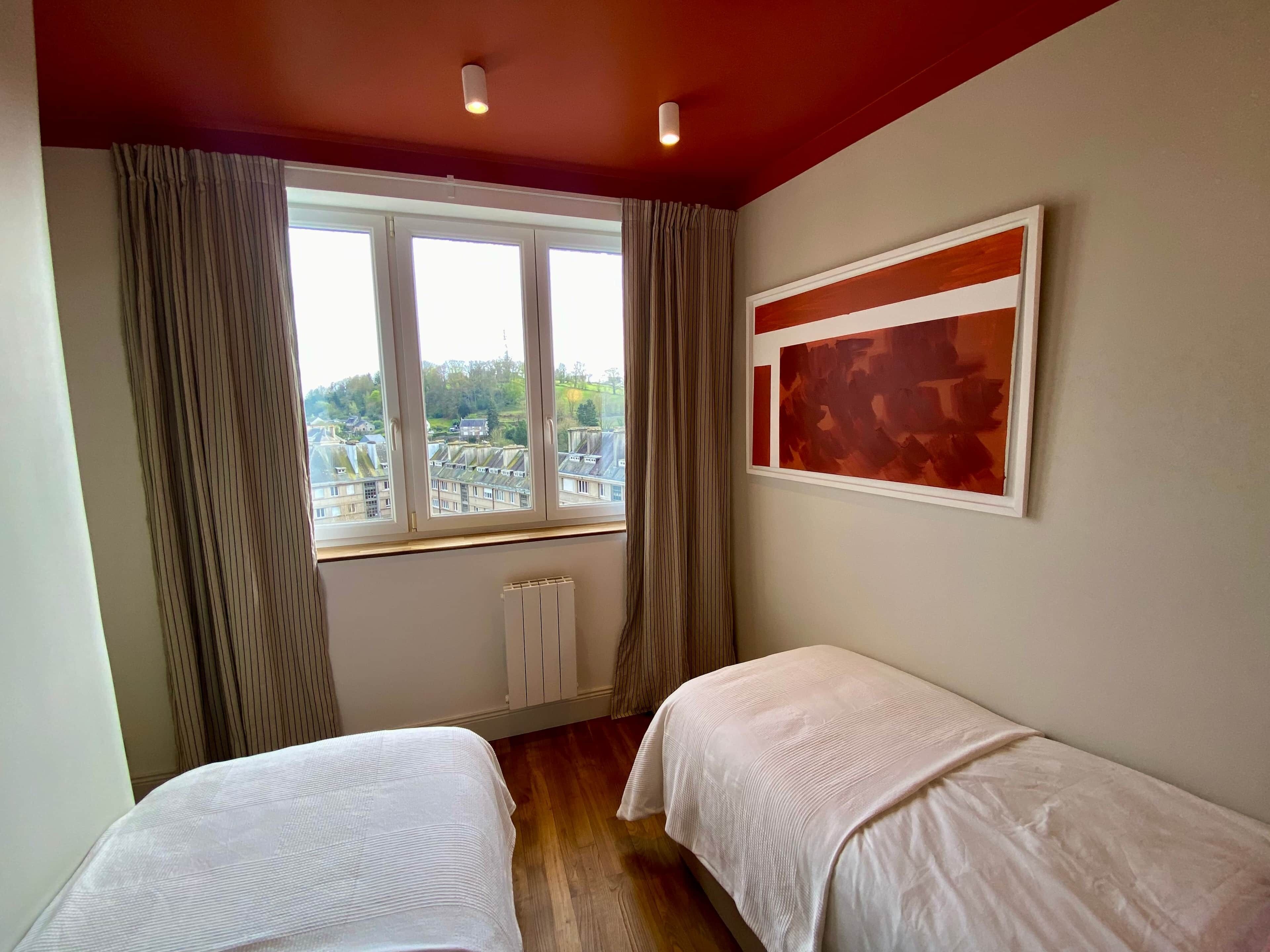 A room with two beds, a window with curtains, a radiator, and a painting on the wall.