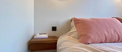 Un dormitori amb un llit, una tauleta de nit i una làmpada de paret.