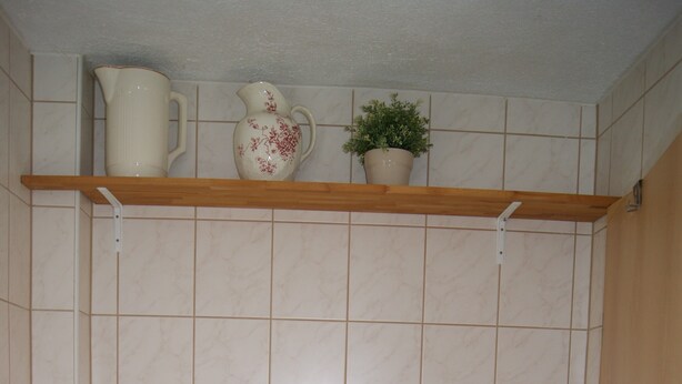 Ein kleines Badezimmer mit Toilette, einem Regal über der Toilette mit Krug und Pflanze sowie einem Wandtrockner.