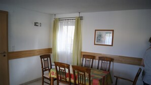 Un coin repas avec une table dressée pour quatre personnes, des chaises en bois, une fenêtre avec des rideaux et un tableau encadré au mur.