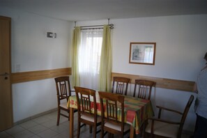 Una zona de menjador amb una taula preparada per a quatre, cadires de fusta, una finestra amb cortines i un quadre al mur.