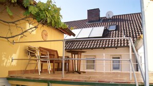 Ein Wohngebäude mit Ziegeldach, Satellitenschüssel, grüner Garagentür und einem kleinen Balkon mit Stuhl und Tisch.