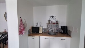 Cocina compacta con microondas, cafetera y un lavamanos pequeño.