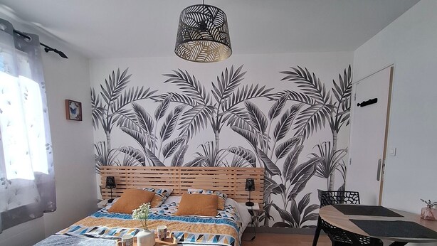 Un dormitorio con cama, una mesa, sillas, una lámpara colgante y una pared con diseño de hojas.
