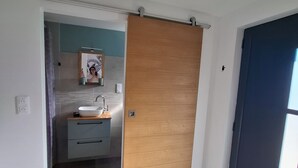 Un baño moderno con puerta de madera, lavabo y espejo.