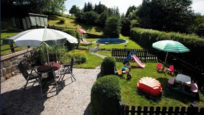 A backyard with a stone patio, outdoor furniture, a slide, and a pool.