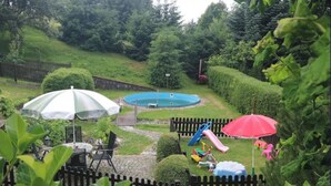 A fenced backyard with a pool, a slide, and two umbrellas.