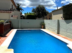 Una piscina rectangular con borde blanco, rodeada por un muro bajo y una planta en maceta.