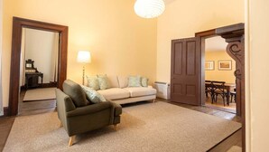 A room with a sofa, a chair, a lamp, and a door leading to another room.