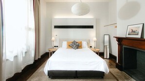 A hotel room with a large bed, bedside lamps, a fireplace, and a framed picture on the wall.