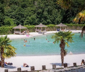 Una playa con agua cristalina, palmeras y una zona de piscina con sombrillas y tumbonas.