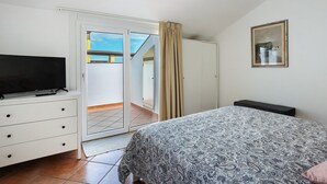 Un dormitorio con cama, televisor sobre una cómoda, armario y puerta corredera que da a un balcón.