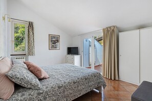 Ein Schlafzimmer mit einem Bett, einem Fernseher, einer Kommode und einer Schiebetür, die auf einen Balkon führt.