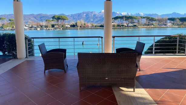 Una terraza cubierta con mobiliario de mimbre, vista a un lago y montañas al fondo.