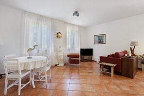 Ein Wohnzimmer mit Esstisch, Stühlen, einer Couch, einem Fernseher und einer Lampe.