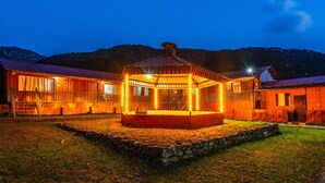 A wooden lodge with a central gazebo, stone walls, and a mountainous backdrop.