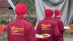 Three individuals in maroon uniforms with 'Yunotri Cottages' branding, carrying trays of food.