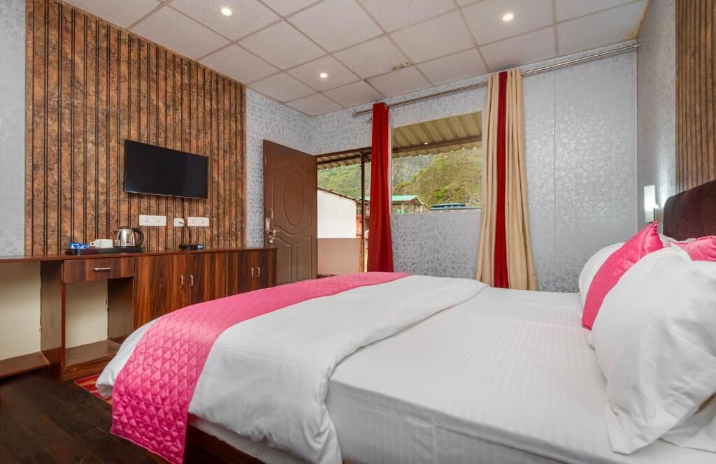Une chambre d’hôtel avec un lit, un téléviseur fixé au mur, un bureau avec une bouilloire et une fenêtre avec des rideaux.