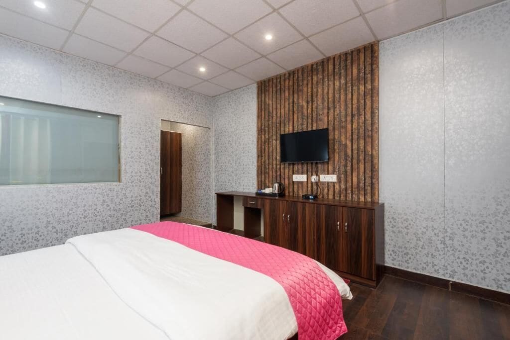 A hotel room with a bed, a TV mounted on a wooden panel wall, a small desk, and a wardrobe.