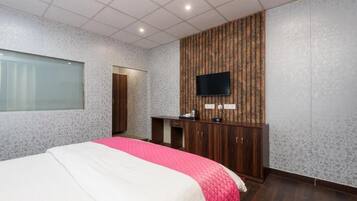 Habitación de hotel con cama, televisor montado en una pared de paneles de madera, escritorio pequeño y armario.