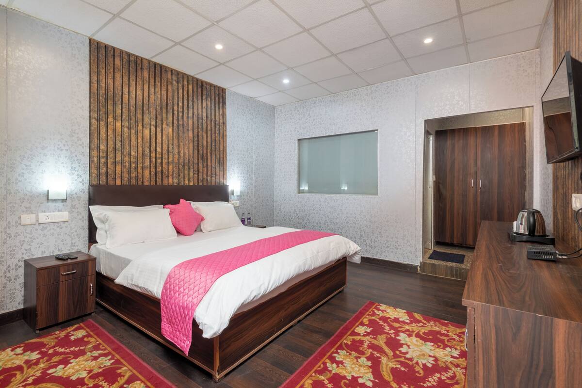 Een slaapkamer met een groot bed, een nachtkastje, een houten garderobe, een spiegel en een rood tapijt.