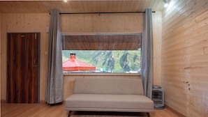 A room with a wooden floor, a sofa, a window with curtains, and a heater.