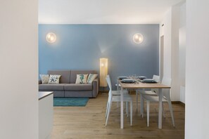 Een moderne woonkamer met een grijze bank, witte stoelen, een houten eettafel en twee wandlampen.