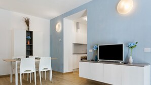 Una cucina moderna con mobili bianchi, un'area pranzo con sedie bianche e un televisore su un mobile bianco.