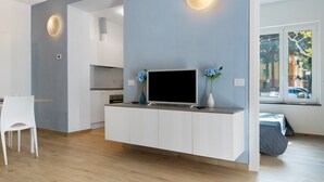 Un soggiorno moderno con una TV su un mobile bianco, una poltrona bianca e vista sulla strada attraverso una finestra.