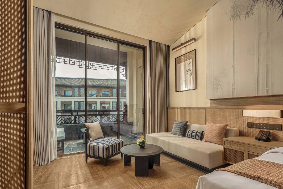 Ein Hotelzimmer mit Balkon, einer Couch, einem Sessel, einem kleinen Tisch und einem Bett.