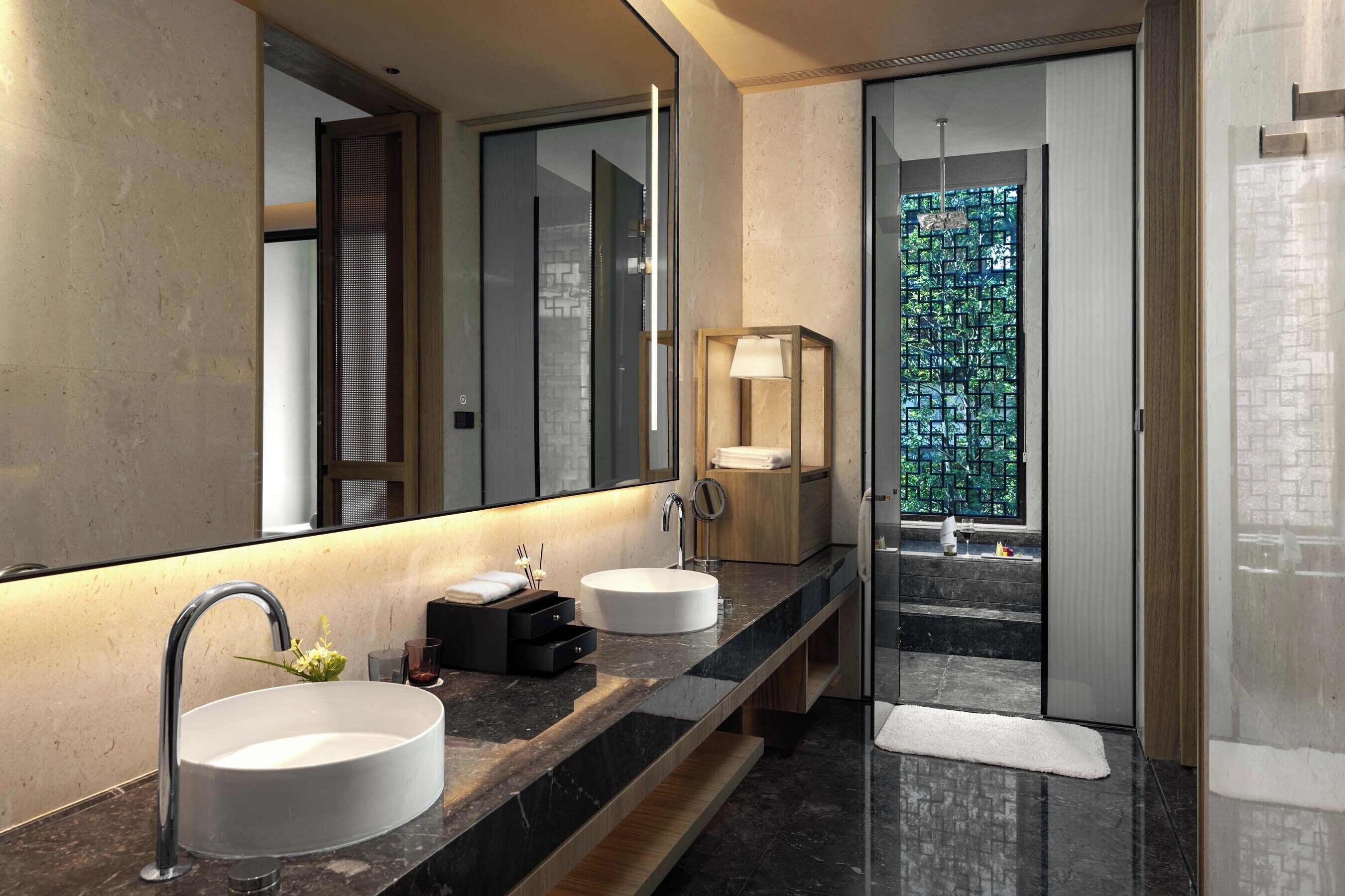 Une salle de bain moderne avec deux vasques, un grand miroir et une vue sur la verdure grâce à une porte en verre.