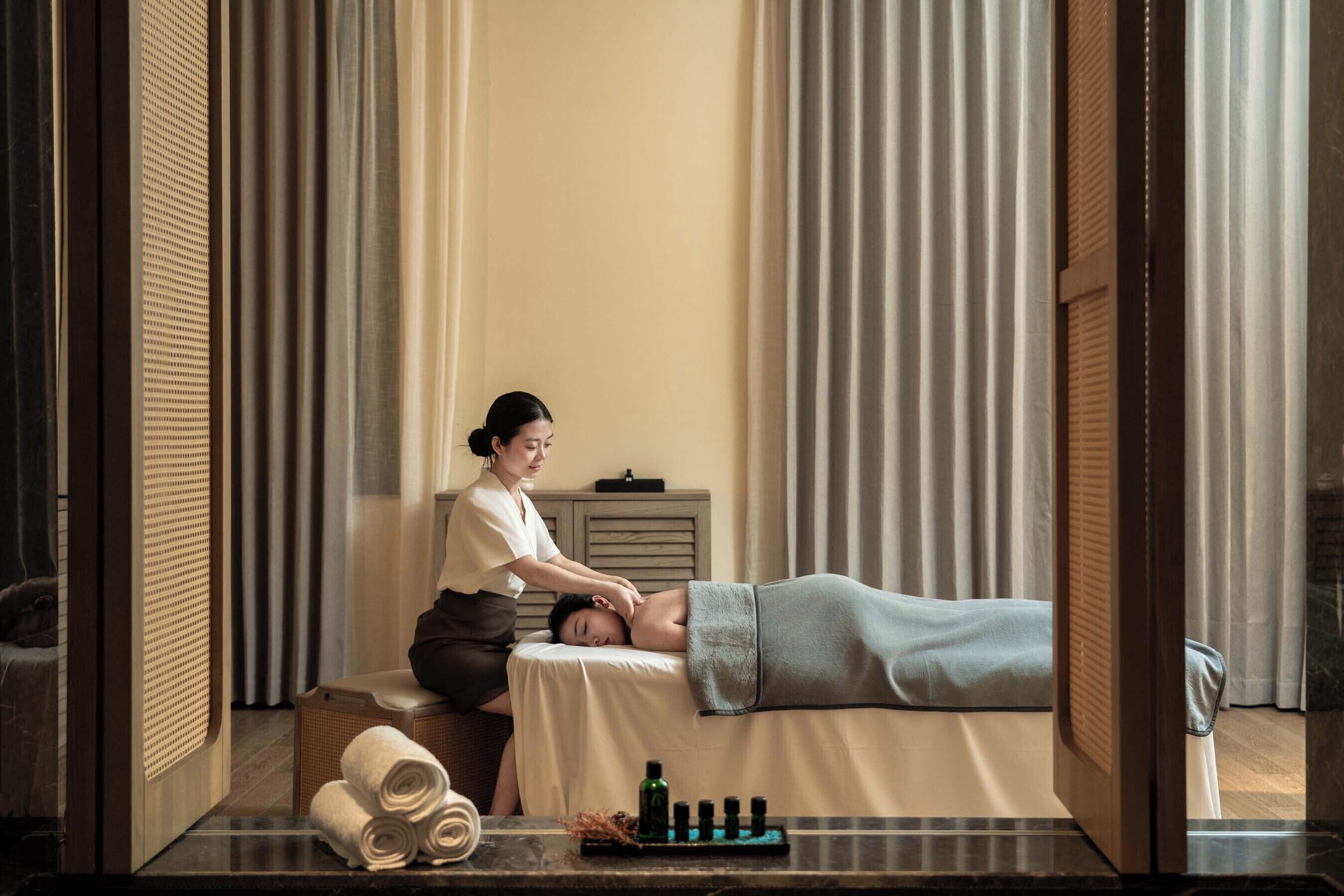 Une salle de massage équipée d’une table de massage, de serviettes, de bouteilles et d’un petit meuble de rangement.