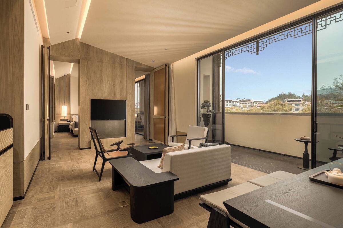 Ein modernes Hotelzimmer mit Balkon, einer Couch, einem Esstisch und einem Fernseher.