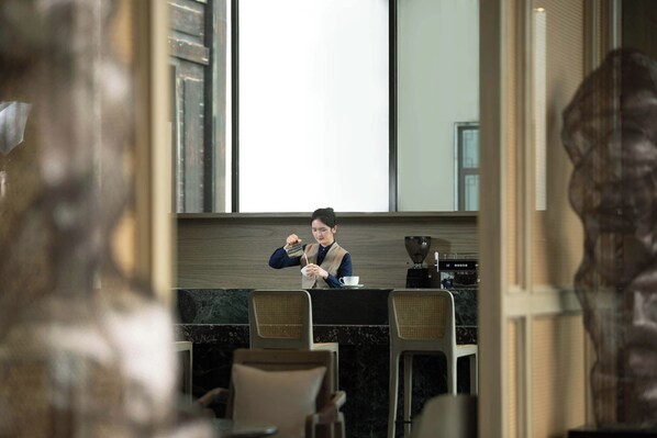 A person at a counter in a room with a large window, a coffee machine, and a marble countertop. - Steigenberger Icons Guizhou Xiaoqikong (Qiannan)