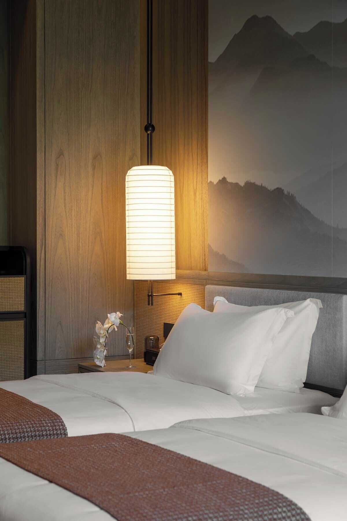 A hotel room with a bed, a nightstand, a lamp, and a wall-mounted picture of mountains.