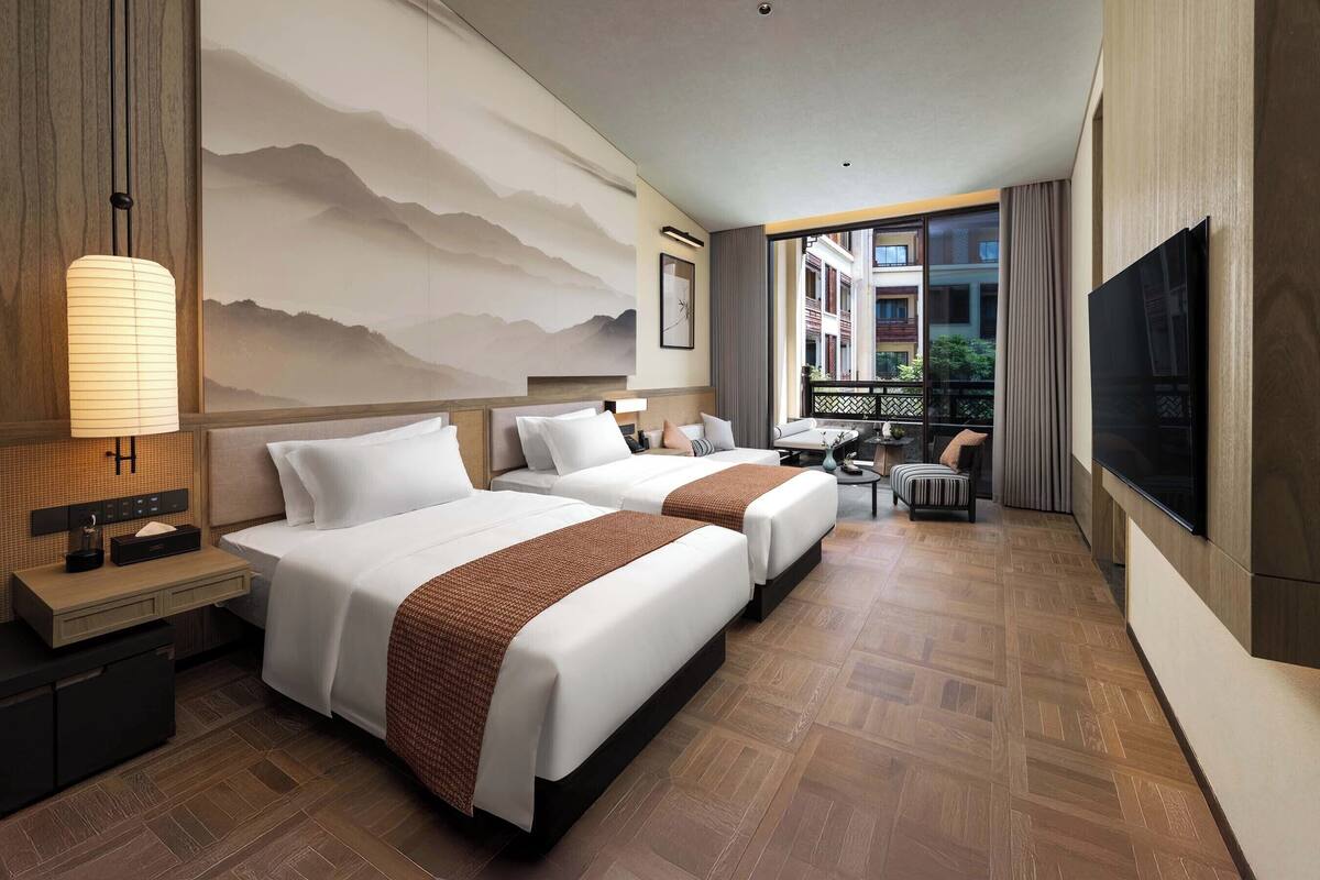 Ein Hotelzimmer mit zwei Betten, einem Fernseher, einem Schreibtisch und Blick nach außen.