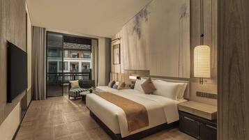 Quarto de hotel com cama, mesa de cabeceira, luminária e vista para um edifício através de uma porta de vidro.